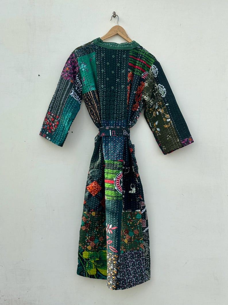 May include: A patchwork robe in shades of green, purple, and red, hanging on a wooden hanger. The robe features a variety of fabric patterns and textures, with a matching belt. The robe is approximately 55 inches long.