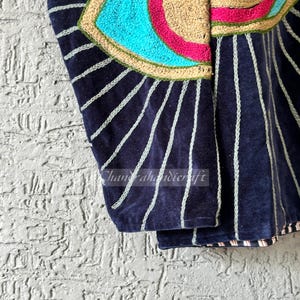May include: Close-up of a navy blue velvet garment with white vertical stripes. The top features an embroidered eye design with turquoise, pink, and tan colors. The text "Chandrahahandicraft" is visible.