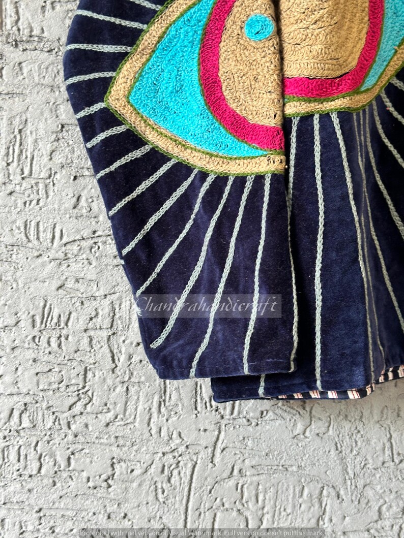 May include: Close-up of a navy blue velvet garment with white vertical stripes. The top features an embroidered eye design with turquoise, pink, and tan colors. The text "Chandrahahandicraft" is visible.