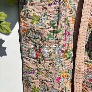 Puede incluir: Una bata beige con estampado floral con un dise&ntilde;o bot&aacute;nico con flores y hojas verdes, rosas y blancas. La bata tiene bolsillos y est&aacute; cosida con hilo rojo. El texto "Chandrahandicraft" es visible.