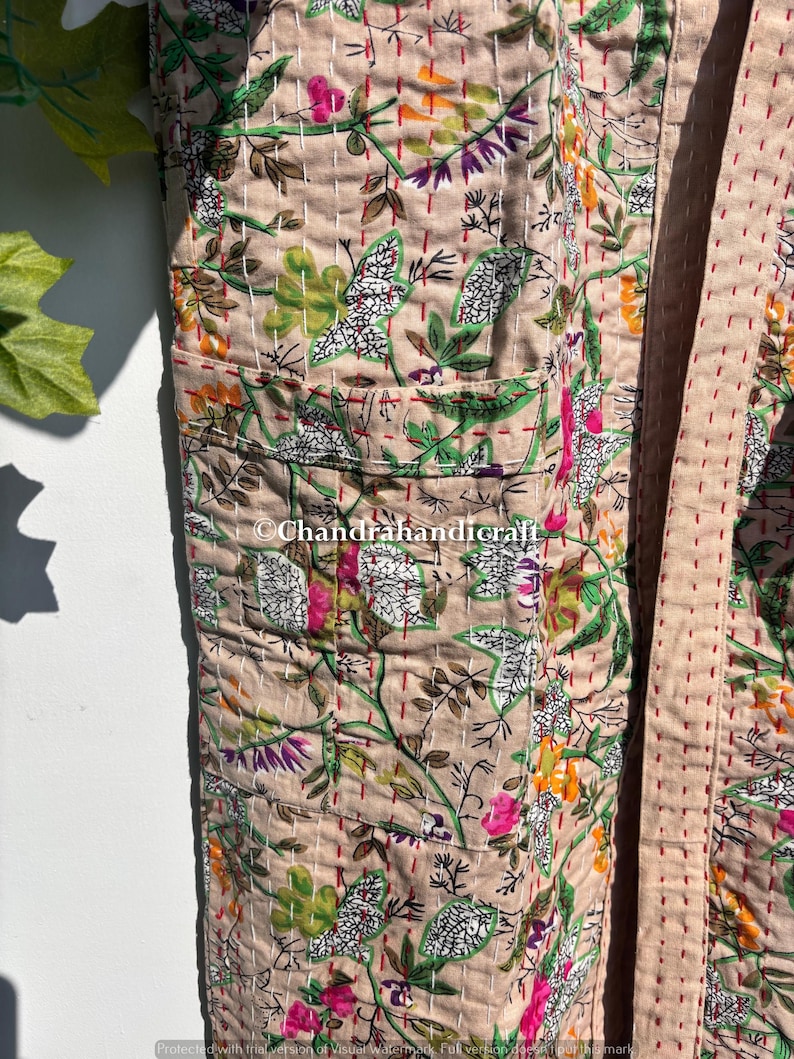 Puede incluir: Una bata beige con estampado floral con un dise&ntilde;o bot&aacute;nico con flores y hojas verdes, rosas y blancas. La bata tiene bolsillos y est&aacute; cosida con hilo rojo. El texto "Chandrahandicraft" es visible.