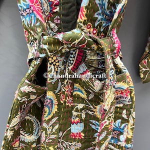 May include: Olive green quilted robe with a vibrant floral pattern in shades of pink, blue, and yellow. The robe features a matching belt and pockets. The stitching is visible throughout the garment, adding texture and detail.