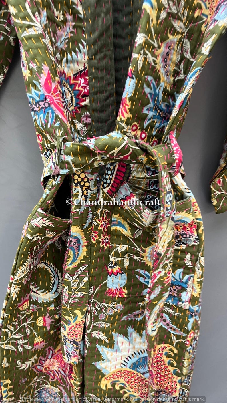 May include: Olive green quilted robe with a vibrant floral pattern in shades of pink, blue, and yellow. The robe features a matching belt and pockets. The stitching is visible throughout the garment, adding texture and detail.
