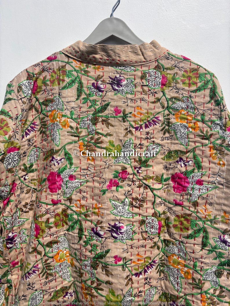 Puede incluir: Chaqueta beige con estampado floral y cuello, colgada de una percha gris. La chaqueta presenta un patr&oacute;n repetido de flores rosas, moradas, naranjas y verdes, con hojas y tallos blancos. Las costuras son rojas.