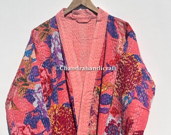 May include: A pink floral patterned robe with a quilted design. The robe features a vibrant mix of red, blue, and purple floral patterns. The robe is hanging on a wooden hanger.