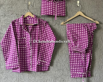 May include: A purple and white checkered pajama set, including a button-down shirt, pants, and a matching pouch, all hanging on wooden hangers against a textured gray wall. The set has white trim.
