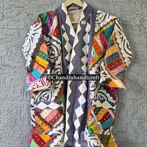 May include: A quilted jacket featuring a patchwork design with multicolored fabric squares in shades of red, yellow, green, and blue, accented by white and dark gray geometric patterns. The garment includes two front pockets and a label reading A6.