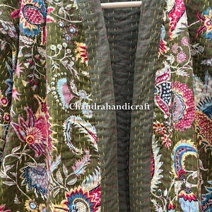May include: Olive green quilted kimono-style jacket with a floral pattern in shades of pink, blue, and yellow. The jacket is hanging on a wooden hanger. The text "Chandrahandicraft" is visible.