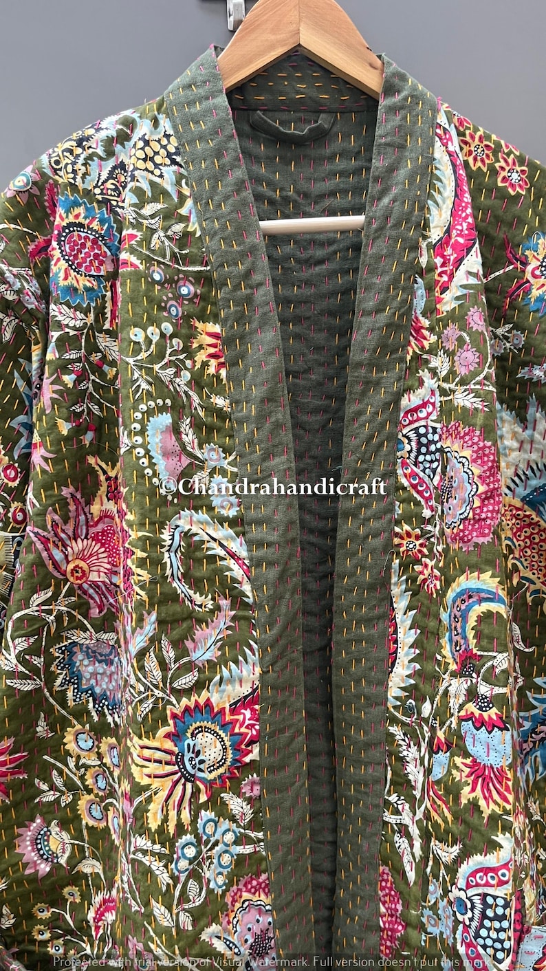May include: Olive green quilted kimono-style jacket with a floral pattern in shades of pink, blue, and yellow. The jacket is hanging on a wooden hanger. The text "Chandrahandicraft" is visible.