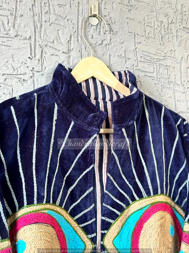 May include: A navy blue velvet jacket with white vertical lines and colorful embroidered details. The jacket has a high collar and is hanging on a wooden hanger. The embroidery includes pink, blue, and tan colors.