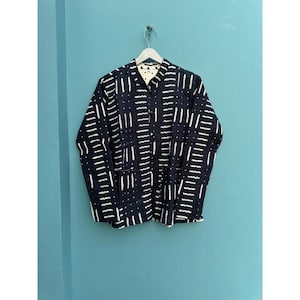 May include: A black jacket with a white geometric pattern of vertical and horizontal lines. The jacket is hanging on a white hanger against a teal wall. The jacket has a collared neckline and button closures.