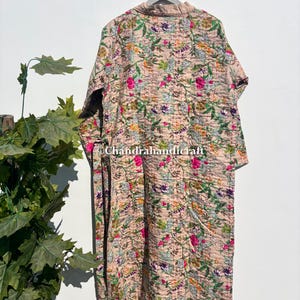 Puede incluir: Larga bata acolchada beige con un estampado floral en rosa, verde, morado y naranja. La bata est&aacute; colgada de una percha de madera. El dise&ntilde;o floral cubre toda la bata.