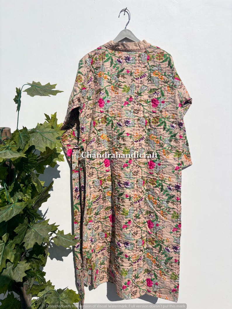 Puede incluir: Larga bata acolchada beige con un estampado floral en rosa, verde, morado y naranja. La bata est&aacute; colgada de una percha de madera. El dise&ntilde;o floral cubre toda la bata.