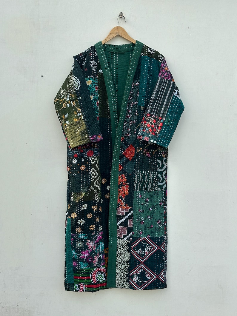 May include: A long, patchwork robe in shades of green, with floral and geometric patterns. The robe is made of various fabric pieces sewn together, with a solid green lining and trim. It hangs on a wooden hanger.
