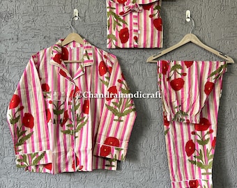 May include: A pink and white striped pajama set with a floral pattern of red flowers and green leaves. The set includes a button-down shirt, pants, and a matching storage bag, all hanging on wooden hangers.