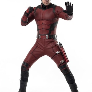 Puede incluir: Una figura con un traje de superhéroe rojo y negro, completo con una máscara con cuernos. El disfraz incluye un body texturizado, guantes, botas y un cinturón de herramientas. La figura posa con una mano levantada.