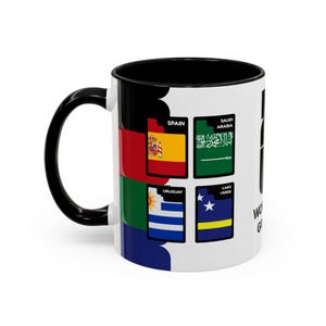 May include: A white ceramic mug with a black interior and handle. The mug features flags of Spain, Saudi Arabia, Uruguay, and Cabo Verde. The words "World" and "Goals" are printed on the side.