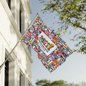 May include: A rectangular flag mounted on a silver pole, featuring a white central panel with the text "2026 WORLD CUP 2026 USA CANADA MEXICO" and a gold trophy icon, surrounded by a repeating pattern of colorful hexagonal national flags.