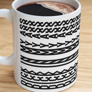 May include: White ceramic coffee mug filled with dark liquid. The mug features a black and white design with the words "MY ASS" in a bold, stylized font, along with various geometric patterns. The mug sits on a light wood surface.