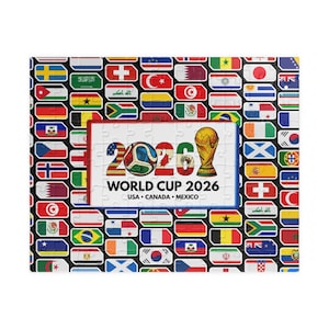 May include: A rectangular jigsaw puzzle featuring a central white panel with the text WORLD CUP 2026 USA CANADA MEXICO, a soccer ball, and a gold trophy. The surrounding border consists of numerous colorful national flags arranged in a grid pattern.