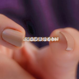 Puede incluir: Una alianza de oro con una hilera continua de piedras redondas, transparentes y de talla brillante engastadas en un canal de metal pulido. El anillo muestra el texto ArtDreamsIN en letras blancas pequeñas en el lateral.