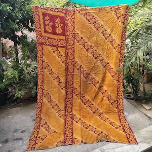 Könnte beinhalten: Ein rechteckiges Textil mit senfgelber Grundfarbe und einem sich wiederholenden dunkelroten Blumenrankenmuster in diagonalen Streifen. Der Stoff enthält einen markanten rechteckigen Abschnitt oben links mit zwei floralen Motiven.