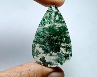 May include: A teardrop-shaped gemstone with a translucent base and intricate green moss-like inclusions. The polished stone is held between fingers, showcasing its natural patterns and color variations. The gemstone is a unique piece of jewelry.