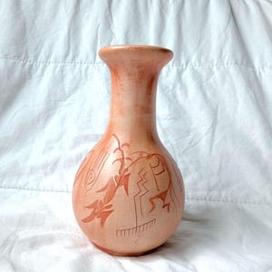 Op de afbeelding: Een perzik-kleurige keramische vaas met een brede basis en een smalle hals. De vaas heeft geëtste ontwerpen van abstracte figuren en plantachtige motieven in een donkerdere perziktint. De vaas staat tegen een witte achtergrond.