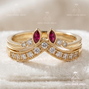 May include: A gold chevron-shaped ring featuring two marquise-cut red rubies at the center peak, surrounded by a row of small round white diamonds along the band. The metal band has a polished finish with delicate milgrain detailing throughout.