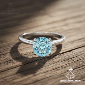 May include: A silver ring with a large, round, light blue gemstone. The ring is set on a wooden surface. The ring is a piece of jewelry.