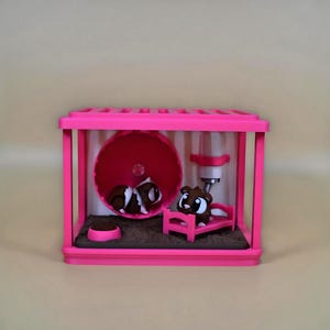 May include: A miniature pink hamster cage with a running wheel, bed, food bowl, and water bottle. Inside are two brown and white hamsters. The cage is a vibrant pink colour.