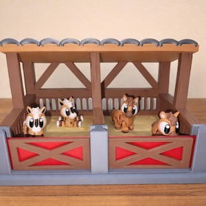 May include: A toy stable featuring four cartoon horses. The stable is brown, grey, and red, with a roof and stalls. The horses are brown and white with large eyes, and are in different poses.