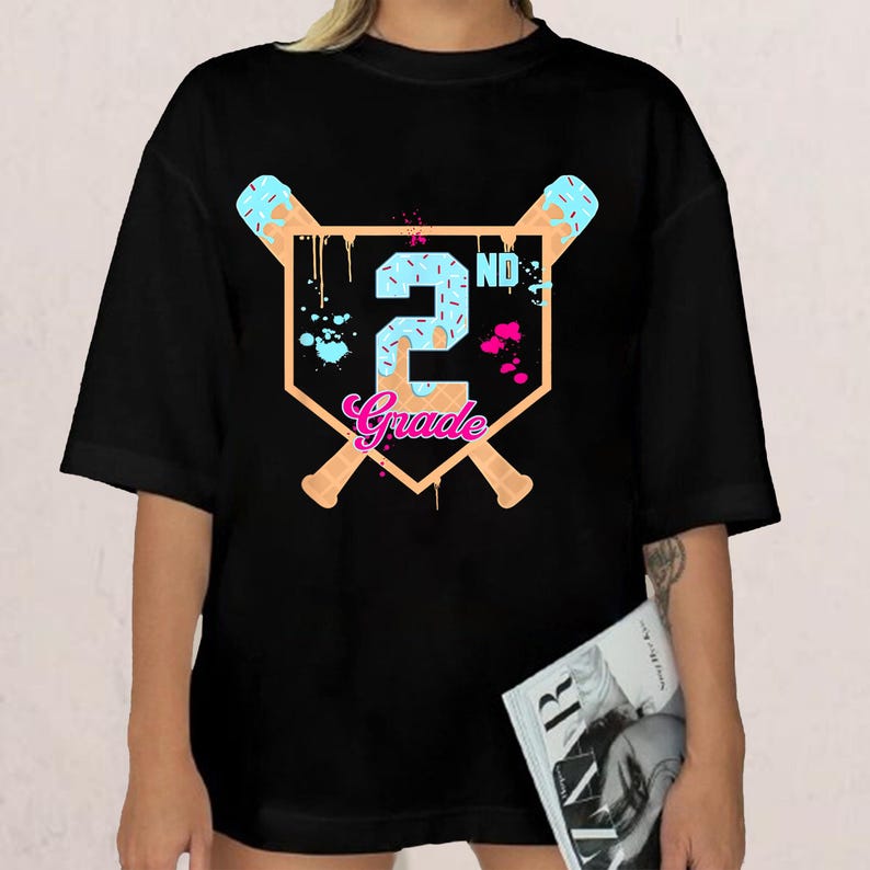 May include: Black t-shirt with a baseball-themed graphic. The design features a baseball diamond shape with crossed baseball bats, the number "2" in blue, and the word "Grade" in pink. The shirt is a casual style.