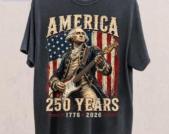 Puede incluir: Camiseta color pimienta con una ilustración de George Washington tocando la guitarra eléctrica frente a una bandera estadounidense. El texto "AMERICA" y "250 YEARS 1776 2026" se muestran en la camiseta.