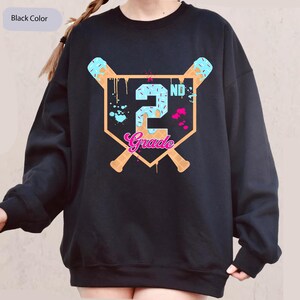 May include: Black sweatshirt with a baseball-themed graphic. The design features a baseball diamond shape with the number "2" and the word "Grade" in a playful font. Two baseball bats and ice cream cones complete the design. The text "Black Color" is in the upper left corner.