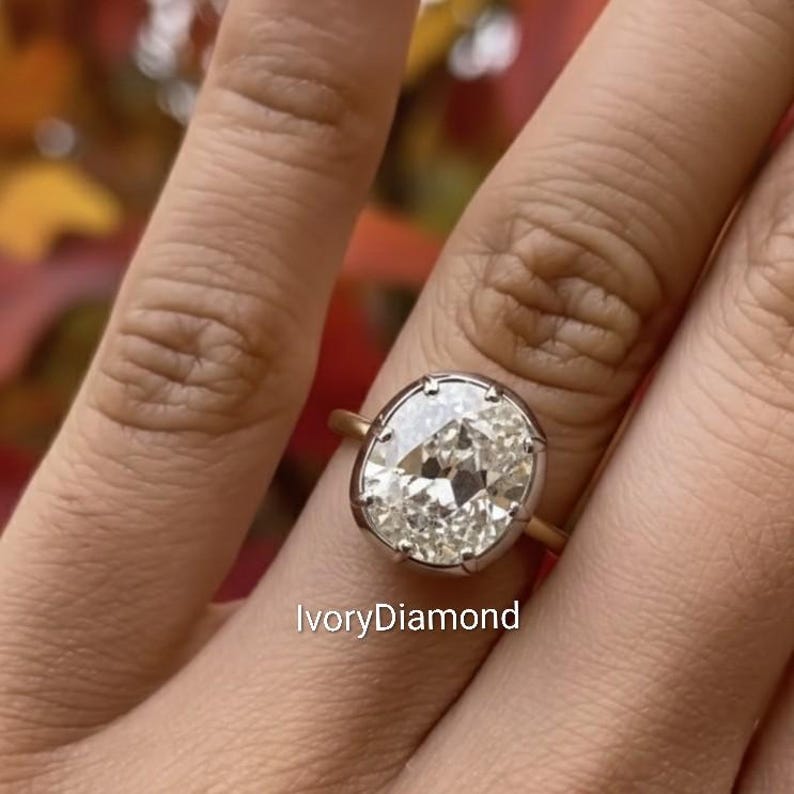 May include: A gold ring with a large, oval-cut diamond. The diamond is set in a bezel setting with a silver-colored metal. The text "IvoryDiamond" is visible at the bottom of the image.