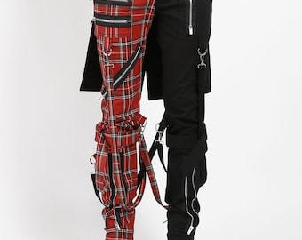 May include: Split-design pants with a red plaid pattern on one leg and solid black on the other. The pants feature multiple zippers, straps, and silver hardware. The model is wearing black platform boots.