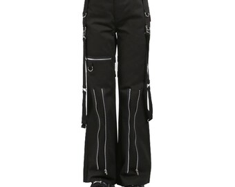 May include: Black pants with silver zippers and straps. The pants have a wide leg design and feature multiple silver metal rings and zippers. The pants are worn with black platform shoes. The pants are a dark, solid color.