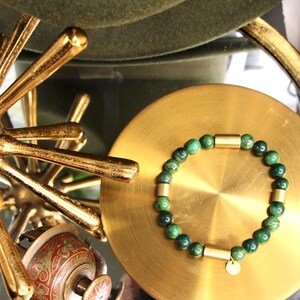 May include: A green gemstone bracelet with gold accents. The bracelet is made of round beads and has a small gold charm.