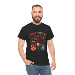 May include: Black t-shirt featuring the text "STARS, STRIPES & SICK BEATS" and musical instrument illustrations. The design includes a guitar, a record, and another guitar, all with red, white, and blue accents. The shirt is worn by a person.