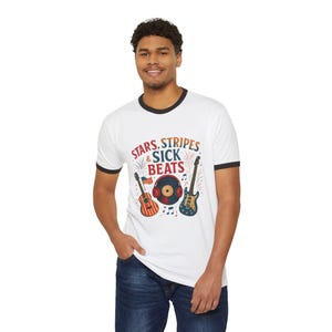 May include: White ringer t-shirt with black trim featuring the text "STARS, STRIPES & SICK BEATS" and illustrations of a guitar, a record, and a guitar. The guitars and record are decorated with patriotic colours.