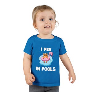 Puede incluir: Una camiseta azul para niños pequeños con el texto "I PEE IN POOLS". La camiseta presenta un gráfico de un gato con gafas de sol en un flotador de flamenco rosa en una piscina. El niño lleva la camiseta.