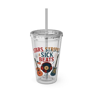 May include: Clear plastic tumbler with a lid and straw. The tumbler has the text "STARS, STRIPES & SICK BEATS" and illustrations of guitars, a record, and headphones. The design uses red, white, blue, and orange colours.