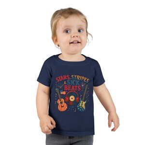 May include: Navy blue toddler t-shirt with the text "STARS, STRIPES & SICK BEATS". The graphic features a red, white, and blue guitar, a record with headphones, and a blue guitar. The design has a patriotic theme.