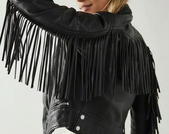 May include: Black leather jacket with long fringe detailing across the shoulders and sleeves. The jacket features a zip closure, snap buttons, and a classic biker jacket design. The model is wearing a white lace dress.