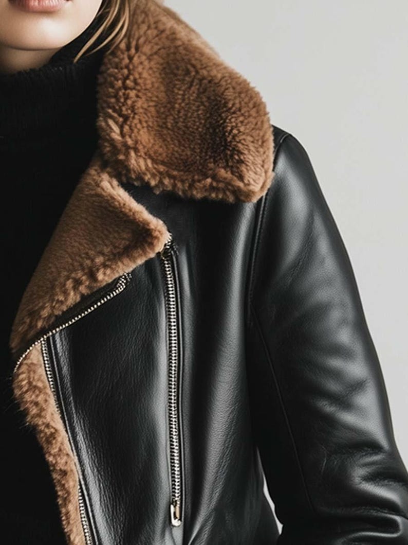 May include: Black leather jacket with a brown shearling collar and lining. The jacket has a silver zip closure and a classic biker design. A stylish outerwear piece.