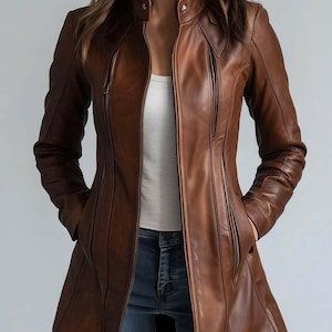 May include: A brown leather jacket with a zip-up front, side pockets, and a stand-up collar. The jacket has a tailored fit and is worn over a white top and blue jeans. The jacket's length extends to the mid-thigh.