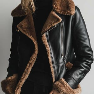 May include: Black leather jacket with a brown shearling collar and lining. The jacket has a zip closure and brown shearling cuffs. The model is wearing a black turtleneck and black trousers.