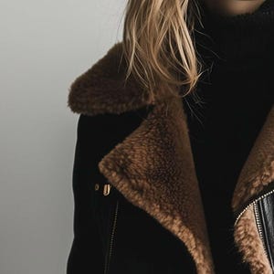 May include: Black jacket with brown faux fur trim and a black turtleneck. The jacket has a zip closure and gold-coloured hardware. The faux fur trim is a warm brown colour.