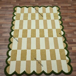 Puede incluir: Una alfombra rectangular con borde festoneado. La alfombra presenta un patr&oacute;n de rayas verticales alternas en beige y blanco. El borde es de color verde oscuro. La alfombra est&aacute; sobre un suelo de madera.